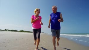 A man and a woman running barefoot on the beach on a sunny day.
