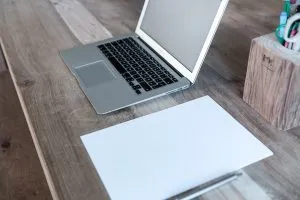 A laptop on a table next to a blank paper.