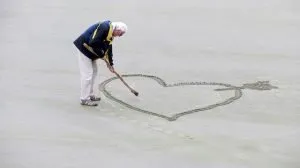 Old man drawing a heart in the sand