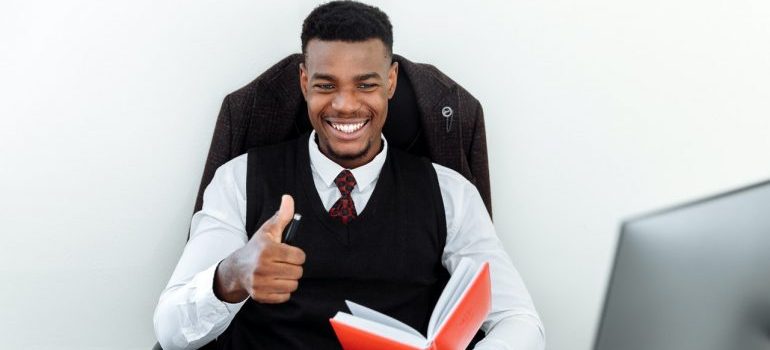 A smiling young man holding a pen and a red book.