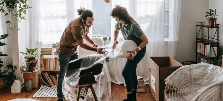 Couple packing a chair in bubble wrap as example that local movers Pompano beach will do that for you