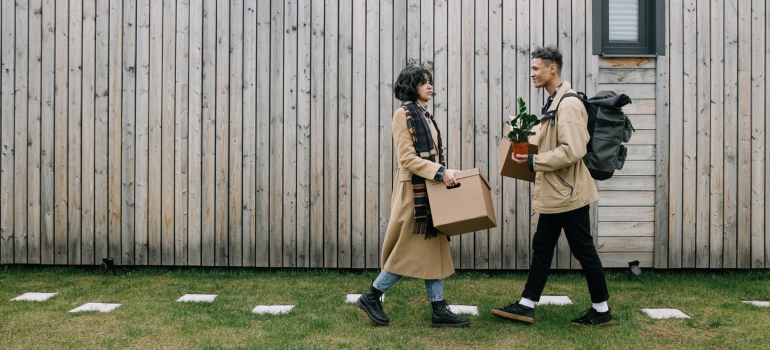 a man and a woman in coats wearing moving boxes across a lawn
