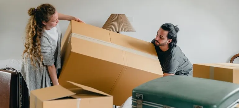 Couple carrying a box and thinking how to choose the right Pompano Beach movers